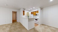 This single-floor residence offers a thoughtful layout that maximizes functionality across its five distinct areas. The combined kitchen and living room serves as the heart of the home, featuring a peninsula-style breakfast bar that separates the kitchen from the carpeted living area. The kitchen is equipped with warm-toned wood cabinetry, white appliances including an electric range and refrigerator, light stone countertops, and recessed lighting overhead. Wood-look flooring runs through the kitchen, adding a clean contrast to the carpeted living space.

The dedicated entrance provides a welcoming transition into the home. The bedroom is a comfortable, well-proportioned room with soft carpeting, a ceiling fan with light fixture, a window with blinds allowing natural light, and a large sliding glass door fitted with vertical blinds. A closet with built-in shelving is accessible from the kitchen area, offering practical storage.

The bathroom is finished with wood-look flooring, warm wood cabinetry beneath a wide vanity mirror, a light stone countertop with a single sink, and a full tub-shower combo with white tile surround. Throughout the residence, a neutral color palette of white walls and beige carpet creates a clean, cohesive ambiance well-suited for comfortable everyday living.
