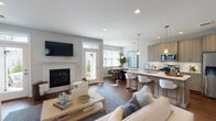 Located at Sutton Landing in Mount Sinai, NY, this thoughtfully designed single-floor home offers a seamless blend of modern finishes and comfortable living. A welcoming entryway with a tray ceiling and rich hardwood flooring leads into the expansive open-concept main living area. The living room centers around a classic fireplace framed by a crisp white mantel, complemented by recessed lighting and direct access to the outdoors through a glass-paneled door. The kitchen is a standout feature, boasting warm wood cabinetry, a large island with quartz countertops and bar seating, pendant lighting, and stainless steel appliances. An adjacent dining area with a stylish chandelier and generous natural light provides an ideal setting for entertaining. The primary bedroom is a serene retreat, featuring plush carpeting, multiple windows with outdoor views, and soft, neutral tones. Additional bedrooms are equally well-appointed, with wide windows that flood each room with natural light and views of the surrounding landscape. The bathroom features elegant marble-style tile surround in the tub-shower combination. The attached two-car garage is finished with an epoxy-coated floor, providing ample storage and parking. Throughout, the home maintains a cohesive, contemporary aesthetic.