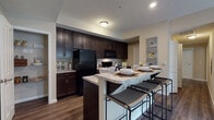 Located at 2845 Austin Manor Boulevard in Columbus, Ohio, this single-floor residence offers a thoughtfully designed layout with a cohesive, contemporary aesthetic throughout. The open-concept kitchen is a standout feature, showcasing rich dark espresso cabinetry, light granite countertops, and black appliances including a refrigerator, range, and built-in microwave. A large kitchen island with bar seating provides an inviting space for casual dining, while an adjacent walk-in pantry offers generous storage. Wood-style flooring flows through the kitchen and living areas, adding warmth and continuity. The living room is bright and welcoming, with sliding glass doors that draw in natural light and provide access to an outdoor area. Two well-sized bedrooms are finished with plush carpet, neutral tones, and natural light from windows with blinds. The primary bedroom features a spacious walk-in closet. Two bathrooms mirror the kitchen's design language, with dark vanity cabinetry, granite-style countertops, and tile flooring. One bathroom includes a walk-in shower with a glass enclosure, while the second serves as a convenient half or guest bath. The overall ambiance is clean, modern, and functional, with a neutral color palette creating a calm and inviting atmosphere throughout.
