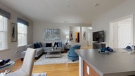 This single-floor residence offers a thoughtfully designed open-concept layout that seamlessly connects the living, dining, and kitchen areas. The living room features warm hardwood flooring, a large sectional sofa, and a generous window that invites natural light, complemented by tasteful wall art and a cozy area rug. Adjacent to the living space, the dining area accommodates a round glass-top table beneath a pendant light fixture, with vertical blinds and draped windows adding an elegant touch.

The kitchen is outfitted with rich dark wood cabinetry, durable countertops, stainless steel appliances including a full-size refrigerator, and tile flooring, offering both functionality and style.

The primary bedroom is carpeted and well-lit by a large window, featuring ample space for a full bedroom suite with coordinated nightstands and framed wall art. The second bedroom similarly offers plush carpeting, a bright window with a decorative valance, and a comfortable, serene atmosphere.

Two bathrooms serve the residence — one featuring a glass-enclosed walk-in shower with clean white tile, and the other a full bathroom with tile flooring and a shower-tub combination. Neutral tones and consistent finishes throughout give the space a cohesive, modern aesthetic.