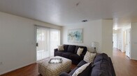 This single-floor residence offers a practical and comfortable layout across several well-defined living spaces. The living room serves as the heart of the home, featuring warm hardwood-style flooring, a textured ceiling, and a sliding glass door fitted with vertical blinds that fills the space with natural light and provides access to the outdoors. The galley-style kitchen is efficiently designed with ample white cabinetry, light wood-style flooring, a double-basin stainless steel sink, a full suite of white appliances including a stove, refrigerator, and dishwasher, as well as generous counter space along both sides. The residence includes multiple bedrooms, each finished with plush carpeting and windows that invite natural light. The primary bedroom is notably spacious with high ceilings and room for generous furnishings, while the additional bedrooms offer comfortable proportions suited for a variety of uses. Two full bathrooms are present in the home, each featuring wood-style flooring, a vanity with a broad countertop and built-in storage, and a shower-tub combination. The overall ambiance of the space is clean, neutral, and functional, with a consistent design palette of light walls and warm flooring tones carried throughout.