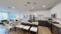 Located within the Harbor Landing community at Garvies Point in Glen Cove, New York, this single-floor residence offers a thoughtfully designed, modern living environment. The open-concept kitchen is a standout feature, showcasing two-tone cabinetry with sleek white upper cabinets and dark wood-grain lower cabinets, a white subway tile backsplash, stainless steel appliances, and a large island with bar seating — ideal for both everyday dining and entertaining. Light wood-tone flooring flows throughout, lending warmth and continuity to the space. The living room is bright and welcoming, benefiting from generous natural light through large windows with horizontal blinds and sheer curtains, creating an airy, open atmosphere. The bedrooms are comfortably scaled, each featuring wide windows that invite natural light, light-toned flooring, and clean white walls that lend a calm, neutral ambiance. The bathrooms are finished with modern fixtures, including a wood-framed vanity mirror, white quartz countertops, and neutral tile flooring, delivering a clean and contemporary aesthetic. An in-unit laundry area adds a layer of everyday convenience. Throughout the residence, the design maintains a cohesive, contemporary style with a bright, neutral palette that creates a polished and comfortable living environment.