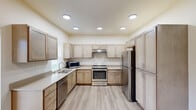 Located at 13809 E Carlisle Ave in Spokane Valley, WA, this single-floor unit offers a clean, contemporary design with a neutral color palette and light-toned luxury vinyl plank flooring throughout the main areas. The expansive kitchen is a standout feature, showcasing light wood cabinetry extending to the ceiling, generous counter space with light quartz countertops, recessed lighting, and a full suite of stainless steel appliances including a range, refrigerator, dishwasher, and microwave. A double-basin sink is positioned beneath a window, offering views of the surrounding greenery. The open layout visible from the dollhouse view connects the kitchen to a spacious living area, providing a comfortable flow throughout the unit. Bedrooms are finished with patterned carpet and feature walk-in closet space, as well as multiple windows that invite natural light and outdoor views. A dedicated laundry closet with a washer is conveniently tucked within the unit. The bathroom is clean and functional, featuring a full soaking tub and shower combination with light vinyl plank flooring. A wall-mounted mini-split unit provides climate control. Overall, the space presents a bright, well-appointed interior suited for comfortable everyday living.