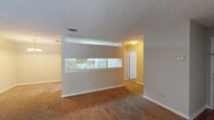 This single-floor residence at 5300 Woodruff Farm Rd in Columbus, Georgia offers a practical and functional layout designed for comfortable everyday living. The open-concept living and dining area is spacious and carpeted, with a textured ceiling and a chandelier that adds a subtle decorative touch. A half-wall pass-through connects this living space directly to the kitchen, promoting an open, airy feel throughout. The kitchen is a galley-style space finished with wood-look hard flooring, white cabinetry providing ample storage, light-toned countertops, a double-basin stainless steel sink, and white appliances including an electric range and a full-size refrigerator. A bathroom features a full-size soaking tub and shower combination with clean white surround walls. The bedroom is generously proportioned, with plush carpet, a ceiling fan with integrated lighting, and a window that allows natural light to filter in. A separate room includes a sliding glass door fitted with vertical blinds, offering a view of the greenery outside and providing additional natural light. Throughout the unit, neutral wall tones and consistent finishes create a cohesive and understated aesthetic suited to a wide range of personal styles.