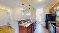 This single-floor residence at 1300 Community Way in Lancaster, Ohio, offers a thoughtfully designed layout that balances functionality and comfort. The entryway opens into a hallway with warm hardwood-style flooring, flush-mount ceiling fixtures, and clean white walls that carry a bright, neutral palette throughout the home.

The kitchen is a standout feature, designed in a galley style with rich cherry-toned cabinetry, dark granite-style countertops, and a suite of black appliances including a refrigerator, electric range with over-the-range microwave, and dishwasher. A double-basin sink sits beneath elegant pendant lighting, and the kitchen connects seamlessly to the living area via a peninsula counter that doubles as a breakfast bar.

The open living and dining area is generously proportioned, featuring the same hardwood-style flooring and crown molding details. A sliding glass door with vertical blinds fills the room with natural light and provides access to an outdoor area. The bedroom is carpeted for added comfort and includes a broad window that allows ample natural light.

The bathroom is clean and functional, featuring hardwood-style flooring, a single-sink vanity with wood cabinetry, a toilet, and a glass-enclosed walk-in shower. A tall window brings in natural light while maintaining privacy. The overall ambiance of this residence is bright, tidy, and move-in ready.