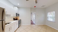 This single-story, one-bedroom, one-bathroom unit offers an efficiently designed layout that maximizes its compact footprint. The kitchen serves as a central feature of the space, finished with light-colored large-format tile flooring and outfitted with white cabinetry, light stone countertops, and a full suite of stainless steel appliances, including a refrigerator, electric range, and over-the-range microwave. Recessed lighting and a ceiling fan overhead keep the kitchen area bright and comfortable, while a exterior door provides convenient access. The open wall adjacent to the kitchen allows the space to feel more expansive than its size might suggest.

The bedroom offers warm-toned hardwood flooring and neutral walls, creating an inviting atmosphere. A window with blinds admits natural light and views of greenery outside, contributing to an airy feel. The room includes adequate wall space for furnishings.

The bathroom is cleanly appointed with tile flooring, a white vanity with a single sink and brushed nickel fixtures, a large mirror, and a glass-enclosed shower, maintaining the consistent, modern aesthetic found throughout the unit. Overall, the space presents a clean, functional, and well-maintained interior.