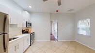 This single-story, one-bedroom, one-bathroom unit offers an efficiently designed layout that maximizes its compact footprint. The kitchen serves as a central feature of the space, finished with light-colored large-format tile flooring and outfitted with white cabinetry, light stone countertops, and a full suite of stainless steel appliances, including a refrigerator, electric range, and over-the-range microwave. Recessed lighting and a ceiling fan overhead keep the kitchen area bright and comfortable, while a exterior door provides convenient access. The open wall adjacent to the kitchen allows the space to feel more expansive than its size might suggest.

The bedroom offers warm-toned hardwood flooring and neutral walls, creating an inviting atmosphere. A window with blinds admits natural light and views of greenery outside, contributing to an airy feel. The room includes adequate wall space for furnishings.

The bathroom is cleanly appointed with tile flooring, a white vanity with a single sink and brushed nickel fixtures, a large mirror, and a glass-enclosed shower, maintaining the consistent, modern aesthetic found throughout the unit. Overall, the space presents a clean, functional, and well-maintained interior.