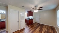 This efficiently designed single-floor, one-bedroom, one-bathroom unit offers a practical and comfortable layout. Throughout the living areas and bedroom, durable wood-look plank flooring adds warmth and visual continuity. Ceiling fans with integrated lighting are present in both the main living area and the bedroom, providing year-round comfort and consistent illumination.

The open living and dining area connects directly to the kitchen, which features rich dark-red cabinetry, dark granite-style countertops, a double stainless steel sink, and black appliances including a full-size refrigerator. A breakfast bar peninsula provides additional counter space and casual seating. A textured ceiling is present throughout the unit.

The bedroom is a well-proportioned, quiet retreat with multiple windows fitted with horizontal blinds, allowing ample natural light while maintaining privacy. The room accommodates standard bedroom furnishings comfortably.

The bathroom includes a full-size soaking tub with an overhead shower, a white surround with built-in shelving, and clean, neutral finishes. Storage is available through closet access visible in the layout.

Overall, this unit presents a functional and well-maintained space with consistent flooring, practical kitchen features, and comfortable living areas suited for everyday use.
