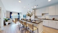 This single-floor residence is designed with a contemporary open-concept layout that seamlessly connects the kitchen, dining, and living areas. The kitchen is a standout feature, outfitted with sleek white cabinetry, dark countertops, a classic subway tile backsplash, and a full suite of stainless steel appliances. A generously sized island with a dark wood-toned countertop provides seating for multiple guests and serves as a natural gathering point. Pendant lighting above the island adds both function and visual interest.

The living area is warm and inviting, featuring light hardwood-style flooring, neutral taupe walls, and large windows dressed with navy drapes that allow abundant natural light to fill the space. The layout flows naturally from the kitchen into this relaxed seating area.

The primary bedroom features large windows with outdoor views, soft carpeting, and a calming neutral palette. A second bedroom showcases a bold blue accent wall paired with ample natural light. The bathroom is clean and functional, finished with white cabinetry, dark countertops, and hardwood-style flooring consistent with the rest of the residence. Throughout, the design balances modern finishes with a warm, livable aesthetic.