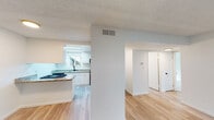 This single-floor unit offers a clean, functional layout designed to maximize comfort and usability. The open-concept living and dining area features light wood-tone laminate flooring throughout, creating a cohesive and airy feel. A textured ceiling adds subtle character to the space, while a wall-mounted thermostat and HVAC vents ensure climate control throughout. The living area is bathed in natural light courtesy of a full-width sliding glass door that opens to a private outdoor patio, enclosed by a wooden fence. The kitchen is thoughtfully designed with white cabinetry, granite-style countertops, a gas range, built-in microwave, and a double sink positioned beneath a window that brings in additional natural light. A peninsula counter with a raised breakfast bar connects the kitchen to the living and dining area, making it ideal for casual dining or entertaining. A skylight above the kitchen entry further brightens the space. The bedroom is carpeted for warmth and comfort, featuring a wide window with views of mature trees and greenery, providing a peaceful, natural backdrop. The full bathroom includes a tub and shower combination with clean white surround, light wood-tone tile flooring, a window for natural ventilation, and sleek matte black hardware accents. Throughout the unit, neutral white walls and abundant natural light create a bright, welcoming ambiance.