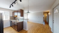 This single-floor residence offers a thoughtfully designed layout that balances functionality with comfort. The open-concept living and dining area is anchored by warm hardwood flooring that runs throughout the main living spaces, complemented by a striking brick-surround wood-burning fireplace that serves as a focal point. Natural light filters through multiple windows fitted with horizontal blinds, creating a bright and welcoming atmosphere. A pendant light and track lighting add layered illumination throughout.

The kitchen is well-equipped with rich dark wood cabinetry, granite-style countertops, a tile backsplash, a stainless steel sink, and black appliances including a range, overhead microwave, refrigerator, and dishwasher. A peninsula with a breakfast bar connects the kitchen to the living area, enhancing the open flow of the space.

The bedrooms feature plush wall-to-wall carpeting and baseboard heating, with one room offering a generous walk-in closet with built-in shelving. The bathroom is finished with warm-toned floor-to-ceiling tile surrounding a tub-shower combination, a wood-vanity with granite countertop, and hardwood-style flooring. A front entry door with a transom window welcomes natural light into the home's foyer.
