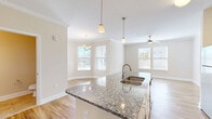 Located at 4005 Galantis Dr in Morehead City, NC, this well-appointed single-floor residence offers a thoughtfully designed layout with one bedroom, two bathrooms, and a range of functional spaces including a pantry, dedicated laundry room, utility room, hallway, and two closets. The heart of the home is an open-concept living, dining, and kitchen area bathed in natural light from multiple windows. The kitchen features a large granite-topped island with a double basin sink, white shaker cabinetry, stainless steel appliances including a refrigerator, range, and microwave, and elegant pendant lighting overhead. Crown molding adds a refined touch throughout the main living areas. The dining area is anchored by a stylish chandelier and benefits from a glass-panel exterior door with transom window, allowing abundant natural light. The spacious bedroom is finished with plush carpet, a ceiling fan, and a window with exterior views. Additional rooms display warm hardwood-style flooring and neutral toned walls throughout. Both bathrooms feature granite vanity tops and tile flooring. The dedicated laundry room comes equipped with a washer and dryer. This residence combines practical amenities with clean, contemporary finishes in a comfortable coastal Carolina setting.