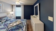 Located at 1011 W Butler Rd in Mauldin, SC, this single-floor residential unit offers a thoughtfully designed layout with multiple bedrooms, a generous living area, a galley-style kitchen, and well-appointed bathrooms. The living room is carpeted and features ceiling fans with light fixtures, large sliding glass doors that provide access to an outdoor area and bring in abundant natural light, and neutral gray walls that create a calm, contemporary atmosphere. The galley kitchen is efficiently arranged with ample cabinetry, a double-basin sink, electric range, and wood-look vinyl flooring that adds warmth and durability. Multiple bedrooms are present throughout the unit, each finished with plush carpeting, ceiling fans, and natural light from windows with blinds and curtain panels. One bedroom features a bold navy accent wall paired with white furnishings, while another includes a walk-in closet and teal-toned décor accents. A third bedroom continues the neutral gray palette with coordinating furnishings. The bathrooms feature wood-look vinyl flooring, vanities with generous counter space, and tub-shower combinations. Textured ceilings and consistent gray wall tones carry throughout the unit, giving the space a cohesive and modern residential feel.