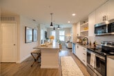 Located at Curry Preserve Drive in Punta Gorda, Florida, this single-floor unit offers a well-designed layout that maximizes every square foot of its compact footprint. The entryway greets visitors with light wood-look flooring and clean white walls, setting a bright, contemporary tone carried throughout the entire space.

The open-concept kitchen and living room serve as the heart of the unit. The kitchen is outfitted with full-height white shaker cabinetry, stainless steel appliances including a refrigerator, electric range, built-in microwave, and dishwasher, complemented by sleek countertops and open shelving for additional storage. The adjacent living area is bathed in natural light through large windows that frame serene outdoor views of the surrounding greenery. A ceiling fan adds both function and style overhead.

The bathroom features a white vanity with granite-style countertops, a spacious walk-in tile shower with glass enclosure, and wood-look flooring that ties seamlessly to the rest of the unit. A dedicated closet provides practical storage.

Crisp white walls, recessed lighting, and consistent light wood flooring unify the space, creating an airy, modern ambiance ideal for comfortable everyday living in the heart of Southwest Florida.