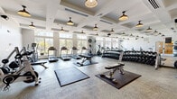 Located at 1125 Westwood Boulevard in Mt. Juliet, Tennessee, this fitness center offers a thoughtfully designed, single-floor workout facility that accommodates a wide range of exercise needs. The space is defined by its striking coffered ceiling, which adds architectural depth and visual interest throughout the room. Rows of stylish pendant lights illuminate the interior, complementing the abundant natural light that pours in through large, floor-to-ceiling windows lining one side of the facility — offering pleasant outdoor views of the surrounding landscape.

The cardio zone is well-appointed with multiple treadmills, elliptical machines, and additional aerobic equipment arranged to take full advantage of the natural light and exterior views. The free weight area features an extensive dumbbell rack reflected by full-length mirrors, enhancing the sense of spaciousness. Adjustable benches and exercise mats are positioned throughout the open floor, supporting a variety of strength and functional training routines.

A dedicated functional training area houses kettlebells, medicine balls, resistance bands, a squat rack, and a plyo box, catering to dynamic and cross-training workouts. Wall-mounted flat-screen TVs provide entertainment throughout the space. The durable speckled flooring is designed for high-traffic use, and the clean, bright aesthetic of white walls contributes to an energizing and motivating workout environment.