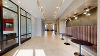 Located at 4500 E 3rd St in Bloomington, Indiana, this contemporary amenity space spans a generous single floor and is designed to offer both comfort and functionality. The welcoming lobby and lounge area immediately sets the tone with large-format light tile flooring, soaring ceilings, and an abundance of recessed and pendant lighting. Clusters of globe pendant fixtures illuminate seating vignettes furnished with tufted leather chairs, a wooden coffee table, and built-in banquette seating with pedestal café tables. A sleek linear fireplace anchors one wall, flanked by tall windows that draw in natural light and outdoor views. A kitchen bar with counter seating and a decorative patterned accent wall adds a social dimension to the living area. Floor-to-ceiling glass doors connect the lounge to the outdoors. The exercise room is well-equipped with treadmills, ellipticals, a cable machine, and a full dumbbell rack, all set on vibrant orange and gray patterned flooring beneath a tray ceiling with a ceiling fan. An accent wall featuring a lively pattern adds visual energy to the space. The recreation room offers a full-size pool table, a large wall-mounted TV set against a bold orange accent wall, and ample natural light through expansive windows.