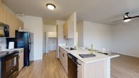 This single-floor space showcases a clean, modern design with consistent light wood laminate flooring flowing throughout the unit, creating a cohesive and airy atmosphere. The kitchen is a standout feature, equipped with light wood cabinetry accented by matte black hardware, white quartz countertops, and black appliances including a refrigerator, electric range, microwave, and dishwasher. A galley-style layout maximizes functionality, with ample upper and lower cabinet storage and a stainless steel sink positioned along the counter peninsula, which also provides space for casual dining.

The living and bedroom areas are generously sized, bathed in natural light through windows fitted with horizontal blinds. The bedrooms feature ceiling fans and wall-mounted heating units, contributing to practical, comfortable living. Neutral white walls throughout the space provide a versatile backdrop adaptable to any decor style.

The bathrooms are distinguished by decorative patterned tile flooring in a classic medallion motif, offering a subtle yet elegant contrast to the otherwise contemporary palette. Light wood vanities with white countertops and chrome fixtures complete the bathrooms. A hallway connects the rooms efficiently, maintaining a straightforward and functional floor plan ideal for everyday living.