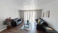 Located at 4301 Lakeshore Dr in Shreveport, Louisiana, this single-story unit offers a well-organized layout across several distinct spaces. The living room serves as the central gathering area, featuring dark hardwood-style flooring, a textured popcorn ceiling, and a large sliding glass door dressed with sheer curtains that allow generous natural light to filter into the space. The open sightlines and neutral gray walls create a clean, versatile backdrop throughout.

The galley-style kitchen is efficiently arranged with white cabinetry lining both sides, dark countertops, a double sink, an electric range, and a dishwasher. Dark hardwood-style flooring continues here, complementing the teal accent wall that adds a touch of color to the space.

The bedroom features wall-to-wall carpet for comfort underfoot, neutral gray walls, a textured ceiling, and a window with blinds that brings in natural light. The room offers ample wall space suitable for various furniture arrangements, and the 3D floor plan scan reveals additional rooms including storage and bathroom access.

The bathroom includes a tub-shower combination with a decorative curtain, a toilet, and hardwood-style flooring, maintaining a consistent aesthetic with the rest of the unit. Overall, the space presents a functional and straightforward layout with a cohesive neutral color palette throughout.