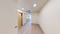Located in the heart of Seattle, WA, The Rise presents a well-designed one-bedroom, one-bathroom unit that maximizes functionality within a compact, efficient footprint. The living area features light-toned luxury vinyl plank flooring and crisp white walls illuminated by recessed ceiling lighting, creating a bright and welcoming atmosphere throughout.

The kitchen is a standout feature, equipped with light maple cabinetry offering ample storage, white appliances including a refrigerator, electric range, and dishwasher, and a functional countertop with a sink. An exposed concrete ceiling in the kitchen area adds an industrial character that contrasts tastefully with the warm wood cabinetry. A window at the end of the kitchen draws in natural light and frames views of the surrounding cityscape.

The bedroom is a clean, open room with the same wood-style flooring and neutral walls, offering a versatile space ready for personalization. An exposed concrete ceiling detail continues here, adding architectural interest.

The bathroom features a light maple vanity with a wide mirror, a white countertop, and durable flooring — all finished in a clean, contemporary style. A light wood door and concrete column accent complete the room's modern aesthetic. The unit's overall design balances urban industrial elements with warm, livable finishes.