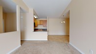 This single-floor residence offers a practical and comfortable layout designed for everyday living. The open-concept living and dining area is anchored by plush wall-to-wall carpeting and warm neutral tones throughout, creating a welcoming atmosphere. A ceiling fan with lighting provides both comfort and illumination, while large windows allow natural light to fill the space and offer views of the surrounding exterior. The galley-style kitchen is accessible via a half-wall pass-through counter, and features warm oak cabinetry, dark granite-style countertops, tile flooring, a stainless steel dishwasher, and a black refrigerator. A utility panel is conveniently located just off the kitchen. The bedrooms are generously sized, each carpeted and fitted with ceiling fans and ample window coverage with blinds for privacy. At least one bedroom includes a closet with direct access. The full bathroom is well-appointed with a tub-shower combination, a vanity featuring dark countertops and wood cabinetry, a large mirror, and tile flooring. A separate water closet provides additional privacy. The overall color palette of soft beige and cream tones lends the space a clean, neutral aesthetic throughout.