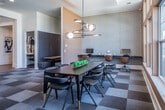 This single-floor business center in Memphis, Tennessee offers a thoughtfully designed professional environment with multiple distinct work areas suited for both collaborative and focused tasks. The space is anchored by a central open area featuring a checkered carpet in muted earth tones, which adds visual depth while maintaining a professional atmosphere throughout.

A standout element is the glass-walled conference room, enclosed by bold black-framed floor-to-ceiling glass panels that allow views into the space from the surrounding areas. Inside, a long conference table is surrounded by ergonomic seating beneath a contemporary multi-globe chandelier, with warm wood wall accents and a teal accent wall enhancing the room's modern aesthetic.

Adjacent to the conference room, a dining or collaborative area features a sleek dark table with gold-accented chairs beneath an artistic branching pendant light fixture. Large multi-pane windows flood the area with natural light and offer views of the surrounding neighborhood.

The workspace also includes semi-private booth seating designed for focused work or small meetings, as well as enclosed individual workstations equipped with desks and task chairs, providing quiet areas for heads-down productivity. A fitness area is visible through a glass-paneled entry, adding wellness-focused amenity to the overall space. The design balances openness with privacy throughout.