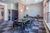 This single-floor business center in Memphis, Tennessee offers a thoughtfully designed professional environment with multiple distinct work areas suited for both collaborative and focused tasks. The space is anchored by a central open area featuring a checkered carpet in muted earth tones, which adds visual depth while maintaining a professional atmosphere throughout.

A standout element is the glass-walled conference room, enclosed by bold black-framed floor-to-ceiling glass panels that allow views into the space from the surrounding areas. Inside, a long conference table is surrounded by ergonomic seating beneath a contemporary multi-globe chandelier, with warm wood wall accents and a teal accent wall enhancing the room's modern aesthetic.

Adjacent to the conference room, a dining or collaborative area features a sleek dark table with gold-accented chairs beneath an artistic branching pendant light fixture. Large multi-pane windows flood the area with natural light and offer views of the surrounding neighborhood.

The workspace also includes semi-private booth seating designed for focused work or small meetings, as well as enclosed individual workstations equipped with desks and task chairs, providing quiet areas for heads-down productivity. A fitness area is visible through a glass-paneled entry, adding wellness-focused amenity to the overall space. The design balances openness with privacy throughout.