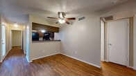 This single-floor residence offers a cohesive and functional layout highlighted by rich, warm-toned hardwood-style flooring that flows consistently throughout every room. The open living area is anchored by a ceiling fan with integrated lighting and connects seamlessly to the kitchen via a raised pass-through counter, creating an efficient and interactive layout. The kitchen is equipped with black appliances, including a coil electric range and refrigerator, complemented by dark cabinetry, granite-style countertops, and an under-cabinet range hood. A door at the rear of the kitchen provides additional access to the exterior. The living space is bright and airy, with natural light entering through large windows fitted with blinds. Multiple bedrooms are present, each featuring ceiling fans, windows for natural light, and hardwood-style flooring. One bedroom includes a walk-in closet, adding practical storage. The bathrooms are consistent in finish, featuring dark wood vanity cabinetry, granite-style countertops, single-basin sinks, medicine cabinet mirrors, and hardwood-style flooring. Textured popcorn ceilings and neutral beige walls are found throughout, lending a uniform and understated aesthetic to the entire unit.