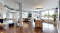 Located at 500–518 Bank St in New London, Connecticut, this thoughtfully designed single-floor space combines contemporary aesthetics with welcoming functionality. The open-plan layout is anchored by rich hardwood flooring throughout, structural columns, and an abundance of natural light streaming in through expansive windows that offer views of the surrounding streetscape.

The main lounge area features a striking stacked-stone fireplace wall with a large mounted television, complemented by curated seating arrangements including plush sofas, armchairs, and ottomans arranged around a marble-topped coffee table. A large communal wooden table with upholstered chairs serves as a central gathering and conference area, ideal for collaboration or casual meetings.

A dedicated kitchenette is outfitted with dark cabinetry, a light quartz countertop, stainless steel appliances, and a vivid teal mosaic tile backsplash. A natural wood plank ceiling and geometric patterned tile flooring lend the space a distinct, artisan character.

A secondary lounge area features a bold blue-toned botanical wallcovering, classic wainscoting, wood-plank ceiling accents, and comfortable mixed seating, offering a quieter retreat within the larger floor plan. Throughout, the space blends industrial elements — such as exposed ductwork — with refined finishes, creating a dynamic and inviting environment well-suited for community engagement and social interaction.