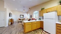 Located in Hesperia, CA, this single-story 2-bedroom, 2-bathroom home offers a well-designed open-concept layout that maximizes every square foot. The combined kitchen and living area serves as the heart of the home, highlighted by soaring vaulted ceilings and a ceiling fan that enhance the sense of airiness. The kitchen features warm honey-oak cabinetry, a white appliance suite including a refrigerator and dishwasher, a peninsula with ample counter space, and direct sightlines into the living area — ideal for both everyday living and entertaining. Arched windows in the living room invite abundant natural light, further brightening the wood-look plank flooring found throughout the main areas. The adjacent dining room benefits from the same elevated ceilings and is anchored by a stylish chandelier. Both bedrooms are carpeted for comfort; the secondary bedroom includes a built-in closet, while the primary bedroom offers a spacious walk-in closet equipped with built-in shelving and hanging rods. Two full bathrooms, each with a tub-shower combination, provide practical functionality. A dedicated closet adds additional storage. The overall ambiance is warm and inviting, with neutral tones and thoughtful architectural details throughout.
