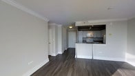 This well-appointed residence at 800 City Tower Apartments offers a thoughtfully designed open-concept layout that seamlessly connects the living and kitchen areas. Dark hardwood flooring runs throughout, providing a rich, elegant contrast to the crisp white walls and bright white baseboards adorned with classic crown molding details. The kitchen is a standout feature, equipped with modern grey cabinetry, stainless steel appliances including a microwave and range, and a granite-topped island with bar seating — ideal for casual dining or entertaining. Track lighting above the kitchen adds focused illumination, while recessed lighting enhances the overall brightness of the space. A clean, neutral color palette of soft greys and whites creates a calm, contemporary ambiance throughout. Additional doorways visible from the main living area lead to separate rooms, hinting at a versatile and functional floor plan. The combination of modern finishes, quality materials, and a cohesive design aesthetic makes this residence a comfortable and stylish urban home within the 800 City Tower Apartments community.