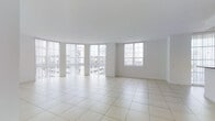 This single-floor space offers a clean, minimalist environment defined by its open layout and bright, airy atmosphere. The interior is finished with large, light-toned ceramic floor tiles that extend throughout, creating a seamless and polished look underfoot. The walls and ceiling are painted in crisp white, enhancing the sense of openness and reflecting natural light throughout the space. A standout feature is the generous window arrangement, including a sweeping curved bank of floor-to-ceiling windows with vertical blinds along one wall, allowing an abundance of natural light to pour in while offering views of the surrounding urban environment. An additional standard window on the adjacent wall further supplements the natural light. The open-plan design provides exceptional flexibility, making the space well-suited for a variety of uses, from commercial or office purposes to creative or event-oriented configurations. The unobstructed floor plan ensures ease of movement and allows for versatile furniture or equipment arrangements. Overall, the space conveys a sense of calm and functionality, with its neutral palette, ample daylight, and well-maintained finishes contributing to a professional and welcoming ambiance.