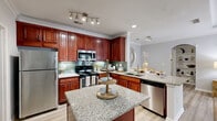 Located at 5375 Sugarloaf Pkwy in Lawrenceville, GA, this well-appointed two-bedroom, two-bathroom residence offers comfortable single-floor living across a thoughtfully designed layout. The kitchen is a standout feature, showcasing rich cherry wood cabinetry, granite countertops, a subway tile backsplash, stainless steel appliances, and a center island with additional counter space — all set atop light hardwood-style flooring. The kitchen flows seamlessly into the living room, which is distinguished by an elegant tray ceiling with crown molding and large French doors that invite abundant natural light and outdoor views. Both bathrooms are well-finished with granite vanity tops, tile-accented tub-shower combinations, and hardwood-style flooring. The spacious primary bedroom features plush carpeting, a ceiling fan, and generous natural light, while the second bedroom offers a similarly comfortable setup. Two closets and two hallways provide ample storage and circulation throughout the unit. A dedicated laundry area with in-unit washer hookups adds everyday convenience. Neutral gray tones and consistent finishes throughout lend the space a cohesive, modern aesthetic suitable for a variety of lifestyles.