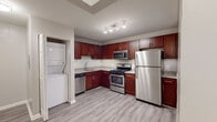 This single-floor residence offers a well-organized layout with a mix of practical and modern finishes. The kitchen serves as a central highlight, featuring rich cherry wood cabinetry extending to the ceiling, granite-style countertops, and a full suite of stainless steel appliances including a gas range, built-in microwave, dishwasher, and refrigerator. A tile backsplash adds a clean, polished detail, while light wood-style flooring ties the space together. Conveniently located adjacent to the kitchen is an in-unit stacked washer and dryer, adding everyday practicality.

The living areas include a generously sized room with neutral carpet and a window providing natural light and outdoor views, making it a bright and comfortable space. An additional room features durable wood-style plank flooring, offering flexibility for various uses.

The bedrooms are carpeted and include closets with built-in wire shelving for organized storage. The bathrooms are well-appointed, with one featuring a floor-to-ceiling dark tile walk-in shower, and another offering a vanity with granite-style countertops and matching cherry wood cabinetry. Throughout, neutral wall tones and consistent flooring choices create a cohesive and move-in-ready environment.
