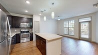 This well-appointed single-floor residence offers a thoughtfully designed open-concept layout that seamlessly connects the kitchen, dining, and living areas. The living space is bathed in natural light through large windows with views of surrounding greenery, complemented by warm hardwood flooring that extends throughout the main areas. A ceiling fan and track lighting add both functionality and style.

The kitchen is a standout feature, equipped with rich dark cabinetry, a tile backsplash, light quartz countertops, and a full suite of stainless steel appliances including a refrigerator, electric range, built-in microwave, and dishwasher. A central island with pendant lighting above provides additional prep space and serves as a natural gathering point.

The bathroom is finished with large-format neutral tiles surrounding a soaking tub and shower combination, accented by a built-in niche for added convenience. Chrome fixtures complete the clean, contemporary look.

A dedicated in-unit laundry room houses a full-size side-by-side washer and dryer, with shelving for storage. The crisp white walls, clean architectural lines, and cohesive design elements throughout create a bright, modern ambiance that is both functional and inviting.