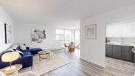 Located on the 12th floor at 75 Bold St in downtown Hamilton, this thoughtfully laid-out 3-bedroom, 2-bathroom unit offers a bright and modern living experience. Light wood-tone flooring flows consistently throughout, lending a clean and cohesive aesthetic to the entire space.

The open living room provides a comfortable and welcoming atmosphere, with ample space for seating and a relaxed layout. It connects naturally to the dining area, which is bathed in natural light from a generous wraparound window configuration that frames sweeping panoramic views of the Hamilton skyline — a true highlight of the unit.

The kitchen is efficiently designed with two-tone cabinetry featuring sleek white upper cabinets and dark wood-grain lower cabinets, complemented by stainless steel appliances including a refrigerator, range, and over-the-range microwave, as well as a clean white countertop.

The primary bedroom is a well-proportioned retreat featuring sliding glass doors that open to a private balcony with city views. The two additional bedrooms offer versatile space suitable for guests or a home office. Two hallways connect the rooms with clean, bright sightlines.

The bathrooms are finished in a crisp, neutral palette. One features a shower-tub combination, while the second offers a more compact layout with wood-tone cabinetry. The unit's overall design prioritizes clean lines, natural light, and urban views.