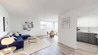 Located on the 12th floor at 75 Bold St in downtown Hamilton, this thoughtfully laid-out 3-bedroom, 2-bathroom unit offers a bright and modern living experience. Light wood-tone flooring flows consistently throughout, lending a clean and cohesive aesthetic to the entire space.

The open living room provides a comfortable and welcoming atmosphere, with ample space for seating and a relaxed layout. It connects naturally to the dining area, which is bathed in natural light from a generous wraparound window configuration that frames sweeping panoramic views of the Hamilton skyline — a true highlight of the unit.

The kitchen is efficiently designed with two-tone cabinetry featuring sleek white upper cabinets and dark wood-grain lower cabinets, complemented by stainless steel appliances including a refrigerator, range, and over-the-range microwave, as well as a clean white countertop.

The primary bedroom is a well-proportioned retreat featuring sliding glass doors that open to a private balcony with city views. The two additional bedrooms offer versatile space suitable for guests or a home office. Two hallways connect the rooms with clean, bright sightlines.

The bathrooms are finished in a crisp, neutral palette. One features a shower-tub combination, while the second offers a more compact layout with wood-tone cabinetry. The unit's overall design prioritizes clean lines, natural light, and urban views.