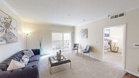 This thoughtfully designed 2-bedroom, 1-bathroom residence offers a comfortable and functional single-floor layout. The living room serves as the heart of the home, featuring plush wall-to-wall carpeting, elegant crown molding, and a large sliding glass door that opens to a private balcony, flooding the space with natural light and providing outdoor access. The open-concept kitchen is equipped with warm honey-toned wood cabinetry, granite countertops, a peninsula with additional counter space, recessed lighting, and hardwood-style flooring. Adjacent to the kitchen, a dedicated dining area with overhead pendant lighting and matching hardwood-style flooring offers an ideal setting for meals. The spacious primary bedroom features soft carpeting, ample closet space, and a calm, neutral color palette. The bathroom is finished with a granite vanity countertop and a framed mirror, lending a polished aesthetic. Throughout the residence, warm beige tones, crown molding, and consistent finishes create a cohesive and inviting ambiance that balances comfort with refined detail.