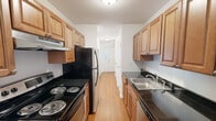 Located at 50 Rinaldi in Poughkeepsie, NY, this one-bedroom, one-bathroom residence offers a well-organized, single-floor layout that makes efficient use of its space. The galley-style kitchen is a functional highlight, featuring warm wood cabinetry, dark granite-style countertops, a stainless steel sink, and a full suite of appliances including an electric range and refrigerator. Light-toned hardwood flooring runs through the kitchen and extends into the hallway, adding warmth and continuity. The living room is bright and inviting, with rich hardwood floors and a sliding glass door that opens directly onto a private patio with outdoor views of green surroundings — an ideal spot for relaxing or entertaining. A wall-mounted air conditioning unit ensures year-round comfort. The bedroom offers a comfortable footprint, carpeted for coziness, and includes a large window that lets in ample natural light with pleasant greenery views. Baseboard heating is present throughout. The bathroom is clean and well-appointed, featuring tile flooring, a combined tub and shower with white subway tile surround, a wood vanity with a stone-top countertop, and classic fixtures. A dedicated closet and hallway with a front entry door complete this practical and comfortable layout.