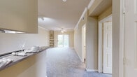 This single-floor residence offers a functional and comfortable layout across two bedrooms and two bathrooms. The open-concept living and kitchen area serves as the heart of the home, where plush carpet, crown molding, and a ceiling fan create a welcoming atmosphere. A sliding glass door with vertical blinds opens to a balcony, filling the space with natural light. Built-in shelving along one wall provides convenient display and storage options. Track lighting illuminates the kitchen, which features a peninsula with a dark-edged countertop, white cabinetry, a stainless steel refrigerator, and hardwood-style flooring that contrasts with the carpeted living area.

The primary bedroom is a comfortably sized retreat with a ceiling fan, a broad window with blinds offering outdoor views, and soft carpeting. The second bedroom mirrors this comfortable design with its own window and carpet flooring. Both bathrooms are similarly appointed, each featuring a tiled shower-tub combination with decorative accent tiles, a white vanity with storage, and wood-style flooring. Two hallways connect the rooms efficiently, contributing to the overall practical flow of this well-designed residence.