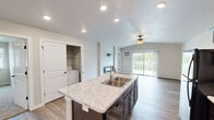 This single-floor residence offers a thoughtfully designed layout across two bedrooms and two bathrooms. The open-concept kitchen and living area serves as the heart of the unit, highlighted by vaulted ceilings and a sliding glass door that leads to a private balcony overlooking a green landscape. Natural light flows freely into the living space, which features wood-look flooring and a wall-mounted electric fireplace as a focal point.

The kitchen is equipped with dark espresso cabinetry, marble-style countertops, black appliances including a refrigerator, range, and microwave, and a central island with a double sink. A dedicated closet near the kitchen houses in-unit laundry facilities. The living area transitions smoothly into the rest of the unit via wood-look flooring throughout common spaces.

The bedrooms are carpeted and include ceiling fans, windows for natural light, and dedicated closets. Each bathroom features dark vanity cabinetry with marble-style countertops and wood-look flooring. The primary bathroom includes a walk-in shower, while the secondary bathroom offers a vanity and toilet. Baseboard heating is present throughout the unit.
