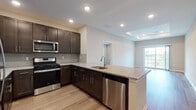 Located at 1 E Pearl Blvd in Burlington, NJ, this well-appointed single-floor residence offers a thoughtfully designed layout with modern finishes throughout. The kitchen is a standout feature, showcasing rich dark-espresso cabinetry, light granite countertops, a large peninsula with an undermount sink, tile backsplash, and a full suite of stainless steel appliances including a gas range, built-in microwave, dishwasher, and refrigerator. Light hardwood-style flooring flows through the kitchen and connects seamlessly to the living area, which benefits from a tray ceiling detail and a sliding glass door that invites natural light and outdoor views. The bedrooms are finished with plush carpeting, recessed lighting, and generous closet space, including a walk-in closet in the primary bedroom. The primary bedroom also features direct access to a private en-suite bathroom with a tiled walk-in shower. A second full bathroom is also present, offering a tiled tub-shower combination and neutral tile flooring. Throughout the residence, a clean, neutral color palette and recessed lighting create a bright, contemporary ambiance suited for comfortable everyday living.