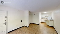 Located at 1920 Ivy Creek Blvd in Durham, NC, this single-floor studio unit offers an efficient, open-concept layout that combines the kitchen and living area into one cohesive space. Light wood-style flooring runs throughout, lending warmth and continuity to the interior. The living area is bright and functional, featuring crisp white walls, a textured ceiling, dark contrasting baseboards, and a window that allows natural light to filter in alongside views of surrounding greenery. A wall-mounted PTAC unit provides convenient in-unit climate control. The kitchen occupies a defined section of the open floor plan and is equipped with white upper and lower cabinetry, a stainless steel single-basin sink, a speckled countertop, and a full-size refrigerator — providing practical storage and food preparation essentials. A recessed closet rod near the entry offers built-in storage, complementing the unit's efficient use of space. The bathroom is cleanly finished with wood-style flooring matching the rest of the unit, white walls, and standard fixtures. Throughout the unit, the design is clean and understated, making it well-suited for straightforward, comfortable living.