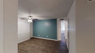 This single-floor residence offers a thoughtfully designed layout with consistent dark hardwood-style flooring throughout, creating a cohesive and polished look across all living areas. The living room serves as a focal point, highlighted by a classic fireplace with a tiled hearth and a bold teal accent wall that adds a pop of color to the otherwise neutral palette. Ceiling fans are featured in multiple rooms, providing both comfort and light. Natural light filters in generously through vertical blind-covered windows in the bedrooms, casting bright patterns across the floors. Each bedroom provides ample space, with one featuring a closet and dedicated ceiling fan. The kitchen is well-equipped with gray shaker-style cabinetry, speckled granite-look countertops, a stainless steel appliance suite including a refrigerator, range, and microwave, plus a double-basin sink and dishwasher. An adjacent dining area with a pendant light and exterior door offers convenient access. The bathroom includes a granite-topped vanity with gray cabinetry, dual framed mirrors, built-in linen storage, and a full tub and shower combination. Textured ceilings are consistent throughout, adding a classic finish to this clean and move-in-ready space.