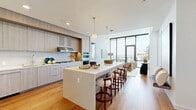 Located in the heart of San Diego at 1331 Columbia Street, this sophisticated two-bedroom, two-bathroom residence offers a refined open-concept layout bathed in natural light. The combined kitchen and living area serves as the centerpiece of the home, anchored by a generous quartz waterfall island with bar seating, light wood cabinetry, a subway tile backsplash, stainless steel appliances, a built-in wine cooler, and globe pendant lighting — all set atop warm hardwood floors. The living room extends seamlessly from the kitchen, with floor-to-ceiling black-framed glass doors opening to a private balcony that frames sweeping views of the San Diego skyline and waterfront. The spacious primary bedroom continues the floor-to-ceiling window design, flooding the room with natural light and panoramic city views, complemented by a dedicated walk-in closet featuring built-in shelving and hanging rails. The en-suite primary bathroom is finished with large-format stone tile flooring, a floating wood vanity, and an illuminated mirror. The second bedroom is bright and well-proportioned, served by a second closet and a clean, modern bathroom. Throughout, the residence maintains a consistent palette of warm neutrals, natural wood tones, and crisp white walls, creating a cohesive and contemporary ambiance.
