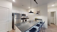 Located at 2211 Dublin Rd in Columbus, Ohio, this single-floor residence offers a thoughtfully designed layout that balances modern style with everyday functionality. The kitchen is a standout feature, showcasing white shaker cabinetry, granite-look countertops, stainless steel appliances, and a peninsula with bar seating — all illuminated by sleek industrial-style pendant lighting and track lighting over wood-look flooring. The living area is warm and inviting, with plush carpeting and French doors that open to an outdoor patio, filling the room with natural light. Two well-sized bedrooms provide comfortable retreats, each with carpeted floors and ample natural light from large windows. The primary bedroom connects directly to a full bathroom and a generously sized walk-in closet fitted with wire shelving for organized storage. A second full bathroom features a soaking tub with shower combination, dark granite-look countertops, white cabinetry, and wood-look flooring. Neutral tones and clean finishes throughout the space create a cohesive, contemporary aesthetic that is both practical and visually appealing.