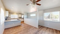 Located at 4497 Fenton Rd in Colorado Springs, Colorado, this single-story home offers a clean, modern aesthetic with a thoughtfully designed layout. The open-concept living and kitchen area is anchored by warm wood-look vinyl flooring and a ceiling fan, creating an inviting, cohesive atmosphere. A half-wall partition subtly defines the two spaces while maintaining an open feel, with multiple windows allowing natural light to flow throughout.

The kitchen is well-appointed with crisp white shaker cabinetry, granite-look countertops, a gray subway tile backsplash, stainless steel appliances including a range, microwave, and refrigerator, and a central island that provides additional prep and seating space. Recessed lighting and plantation shutters add a polished touch.

The bedrooms feature plush carpeting, ceiling fans, wall-mounted mini-split HVAC units for individual climate control, and windows with exterior views. The primary bedroom includes two interior doors, suggesting access to a closet and an en-suite or hallway. A full bathroom is finished with wood-look flooring, white cabinetry with granite countertops, a single-basin sink, and a tub-shower combination. The home's neutral color palette and consistent finishes create a cohesive, move-in-ready environment throughout.