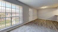 Located at 10500 Valley Forge Dr in Houston, TX, this single-floor residence offers a thoughtfully arranged layout that balances comfort and functionality. The living area makes a strong architectural statement with a full white-painted brick accent wall that adds texture and character to the space. Plush gray carpet covers the living and bedroom areas, while wood-look plank flooring runs through the entryway and kitchen, creating a clean visual transition between spaces. Large windows with vertical blinds allow natural light to fill the interior and provide views of the surrounding outdoor area.

The kitchen is equipped with granite-style countertops, dark cabinetry, a dishwasher, and a full-size refrigerator, offering ample storage and prep space. The primary bedroom is generously sized, featuring a ceiling fan with light fixture, carpeted flooring, and access to a dedicated en-suite bathroom. The bathroom is appointed with a wide vanity topped with granite-style counters, dark wood cabinetry, and wood-look tile flooring. Additional closet space is accessible directly from the bedroom. The neutral gray wall palette throughout the unit creates a clean, cohesive aesthetic that is both modern and versatile.