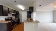 This single-story residence offers two bedrooms and two full bathrooms within a thoughtfully arranged floor plan. The kitchen is a standout feature, designed in a galley style with dark espresso cabinetry lining both walls, granite-look countertops, and stainless steel appliances including an electric range, refrigerator, and dishwasher. A peninsula with a built-in sink extends toward the living area, creating a natural division between the kitchen and adjoining spaces. Wood-look flooring runs throughout the kitchen, while carpet covers the living areas and bedrooms.

The living room is highlighted by a tray ceiling with crown molding, a ceiling fan, a tile-surround fireplace, and a sliding glass door that opens to an outdoor balcony, allowing natural light to fill the space. Both bedrooms are carpeted and generously sized, with the primary bedroom offering direct access to an en-suite bathroom. Each bathroom features dark cabinetry with granite-look countertops, a tub-shower combination with white tile surround, and wood-look flooring, providing a cohesive and practical finish throughout the home.