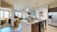 This thoughtfully designed 2-bedroom, 3-bathroom single-floor residence offers a comfortable and functional layout with modern finishes throughout. The entryway, finished with rich hardwood-style flooring, opens into a seamless kitchen and living area. The kitchen is a standout feature, showcasing dark espresso cabinetry, granite countertops, stainless steel appliances, and a large central island with bar seating — all illuminated by stylish pendant lights and a track lighting system. The open-concept living room is bright and welcoming, with crown molding, a ceiling fan, and a glass door leading to an outdoor patio with green space views. Both bedrooms are carpeted and well-proportioned, each with dedicated closet space. The primary bedroom includes a walk-in closet with built-in wire shelving. The three bathrooms are elegantly finished with dark wood vanities, granite countertops, hardwood-style flooring, and a mix of a soaking tub and a glass-enclosed walk-in shower. Two spacious closets provide ample storage throughout the residence. The warm, neutral color palette and consistent finishes create a cohesive and inviting ambiance from room to room.