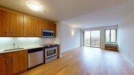 Located at 550 Locust St in Mount Vernon, NY, this well-appointed single-floor residence combines modern finishes with a thoughtful, open layout. Rich hardwood flooring flows throughout the main living areas, lending warmth and continuity to the space. The open-concept living and dining area is bright and airy, benefiting from abundant natural light streaming through a large sliding glass door that leads to a private balcony with scenic outdoor views — a standout feature of the home.

The kitchen is efficiently designed with warm wood cabinetry, a white tile backsplash, and a full suite of stainless steel appliances, including a refrigerator, dishwasher, range, and built-in microwave. It opens seamlessly into the main living area, making it ideal for everyday functionality.

The bedroom offers a quieter retreat, finished with plush carpeting, a wall-mounted HVAC unit, and a window that allows natural light to filter in. Ample closet space is also available. The bathroom is finished with neutral large-format tile surrounding a full soaking tub and tub surround, offering a clean and classic aesthetic.

A practical in-unit stacked washer and dryer is conveniently accessible, adding to the home's overall functionality. Clean white walls and consistent trim throughout give the space a fresh, move-in-ready appeal.